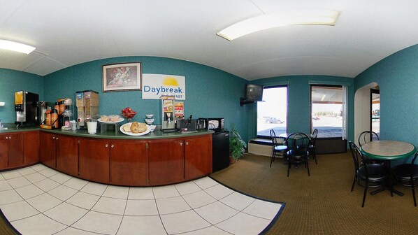 A reception area with a curved counter, a Daybreak sign, a coffee station, and a seating area with chairs and a table.