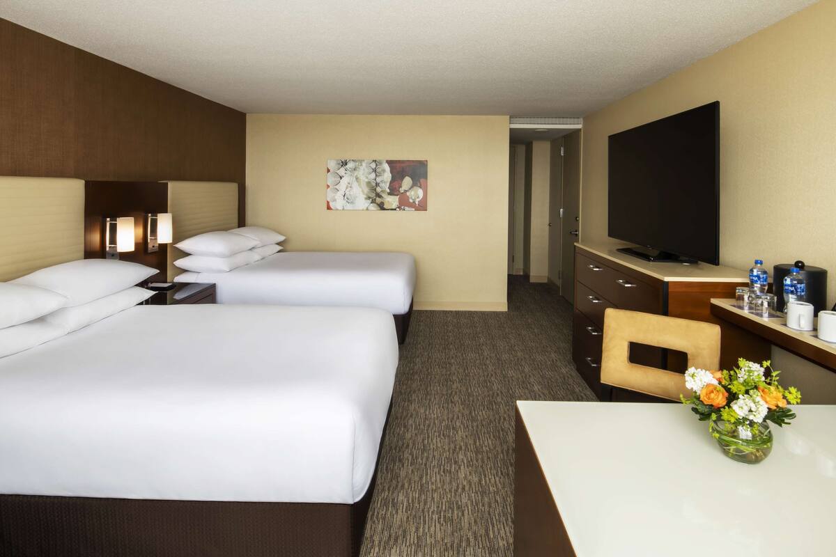 A hotel room with two beds, a TV, a desk, and a vase of flowers.