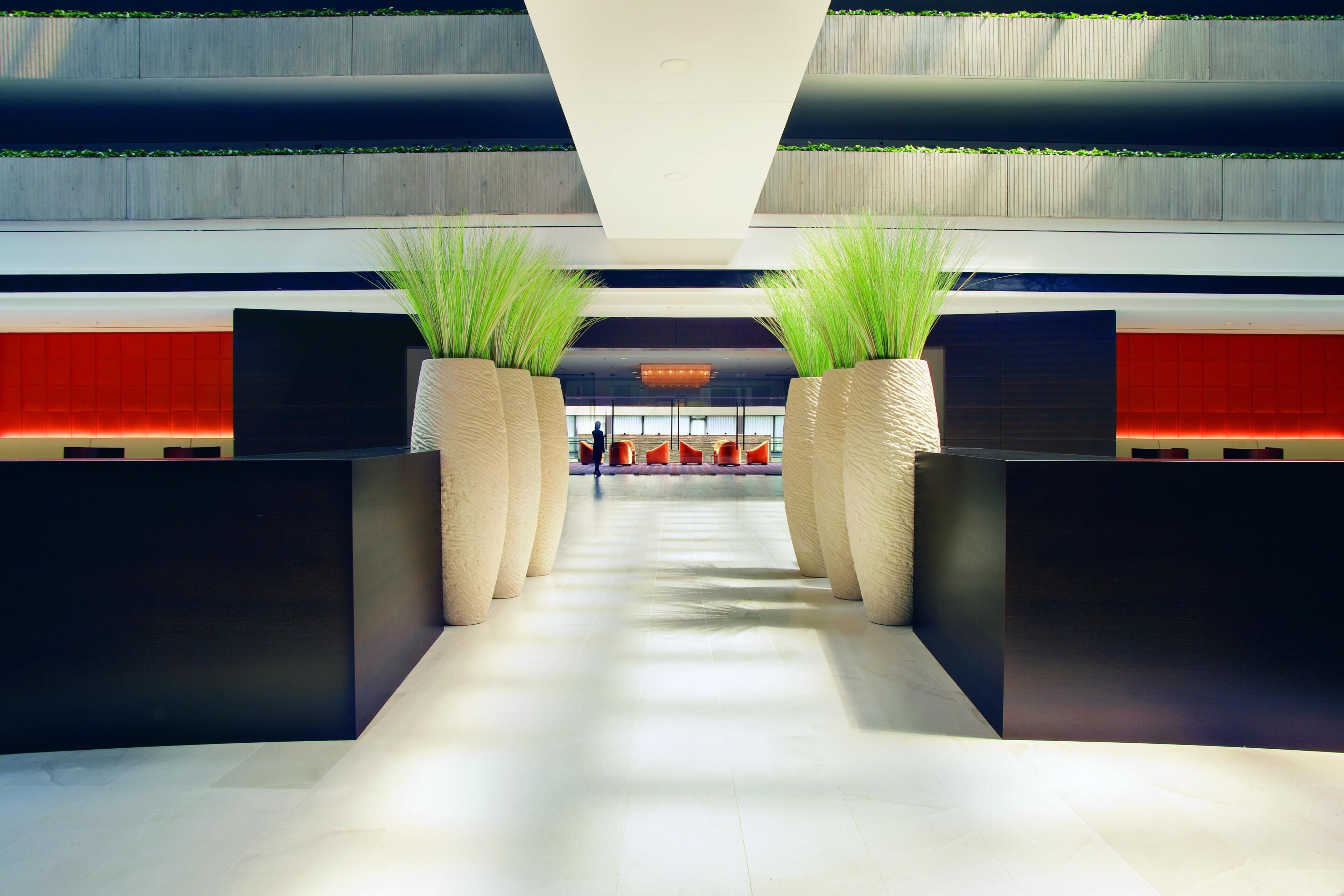Een moderne lobby met een centrale doorgang, twee receptiebalies en een zithoek op de achtergrond.