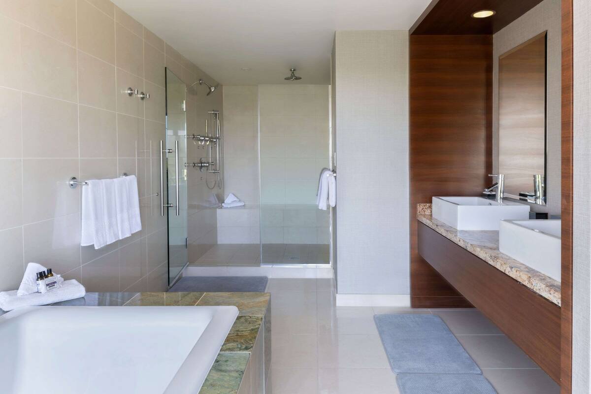 A modern bathroom with a glass-enclosed shower, a large bathtub, and a vanity with two sinks.