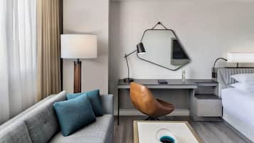 Habitación de hotel con sofá, escritorio, silla, cama, lámpara y espejo.