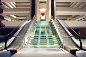 A modern interior with two escalators leading to a central staircase with glass steps. - Hyatt Regency O'Hare Chicago (Rosemont)