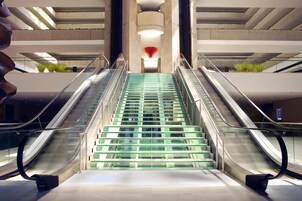 A modern interior with two escalators leading to a central staircase with glass steps.