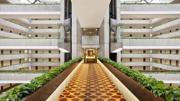 A multi-level atrium with a central walkway, glass railings, and greenery.