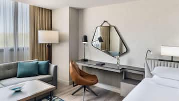 Habitación de hotel con sofá, escritorio, silla, cama, espejo y lámpara.