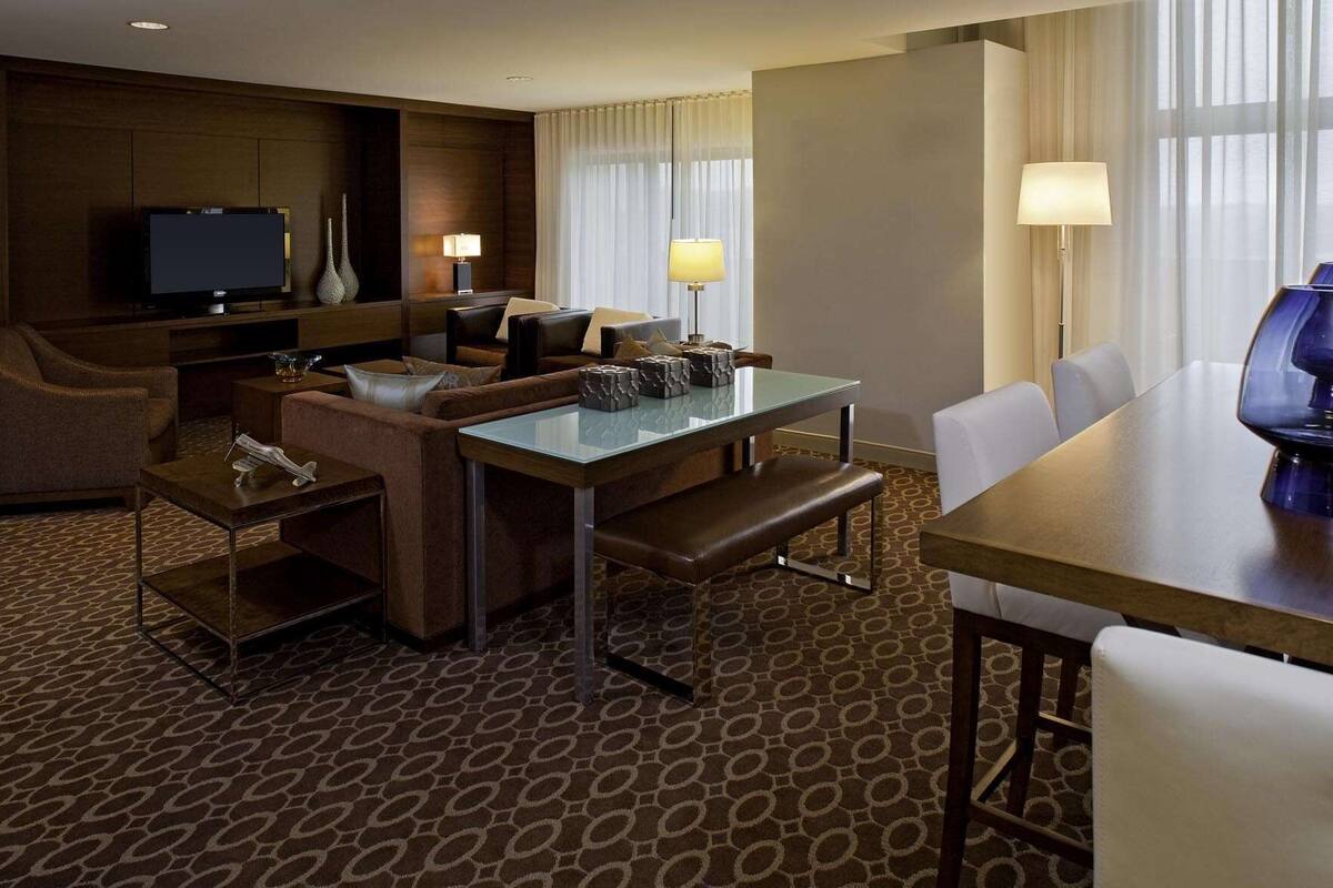 A hotel room with a sofa, a dining table, a TV, and a lamp.