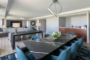 A modern hotel room with a dining area featuring a marble table and blue upholstered chairs, a kitchen with a coffee machine, and a large mirror on the wall. - Hyatt Regency O'Hare Chicago (Rosemont)