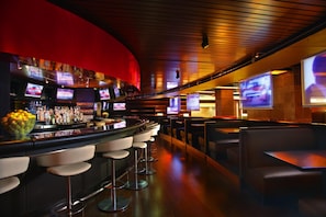 A bar area with a curved counter, multiple screens, and seating. - Hyatt Regency O'Hare Chicago (Rosemont)