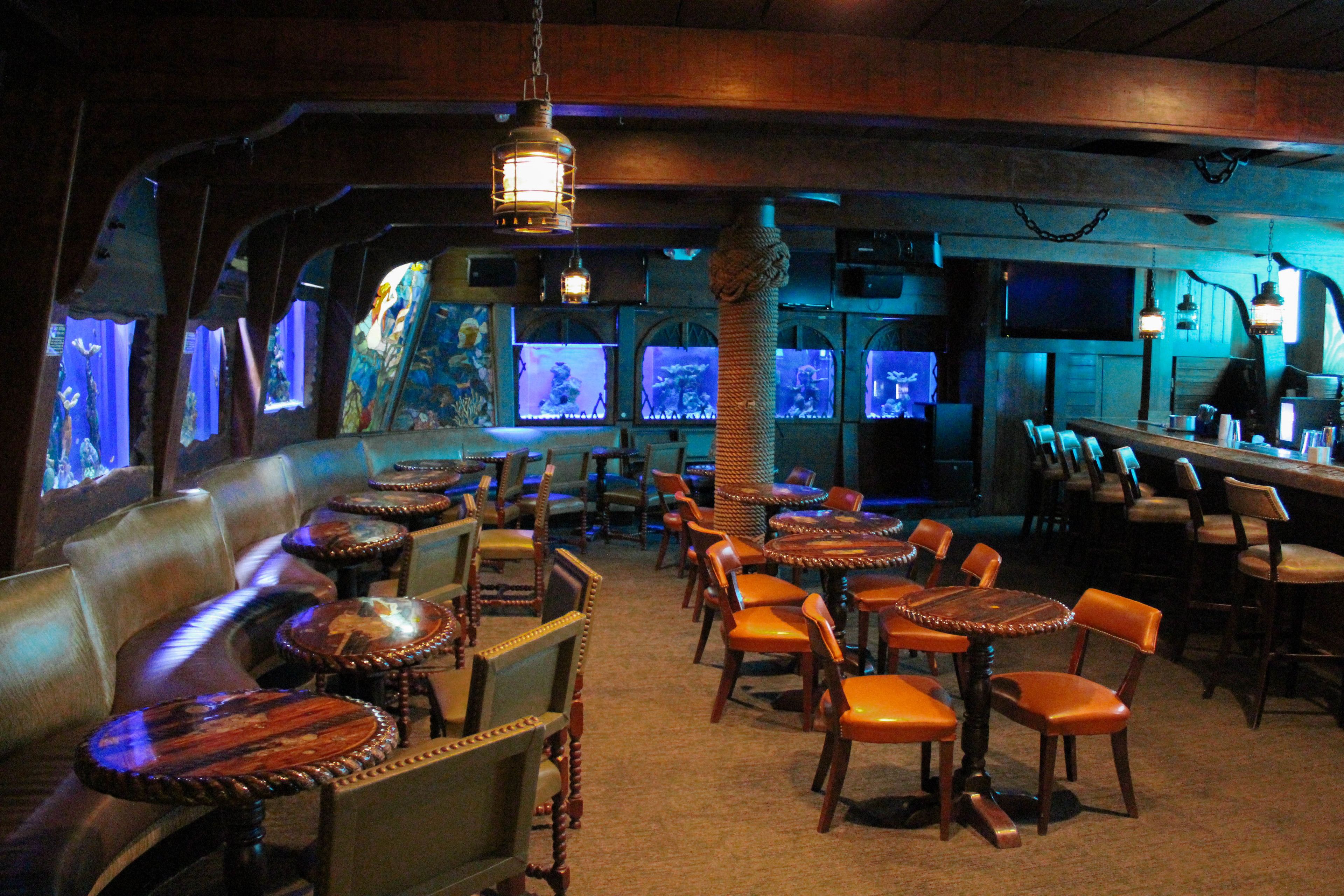 A bar area with leather seating, wooden tables, and aquarium displays.
