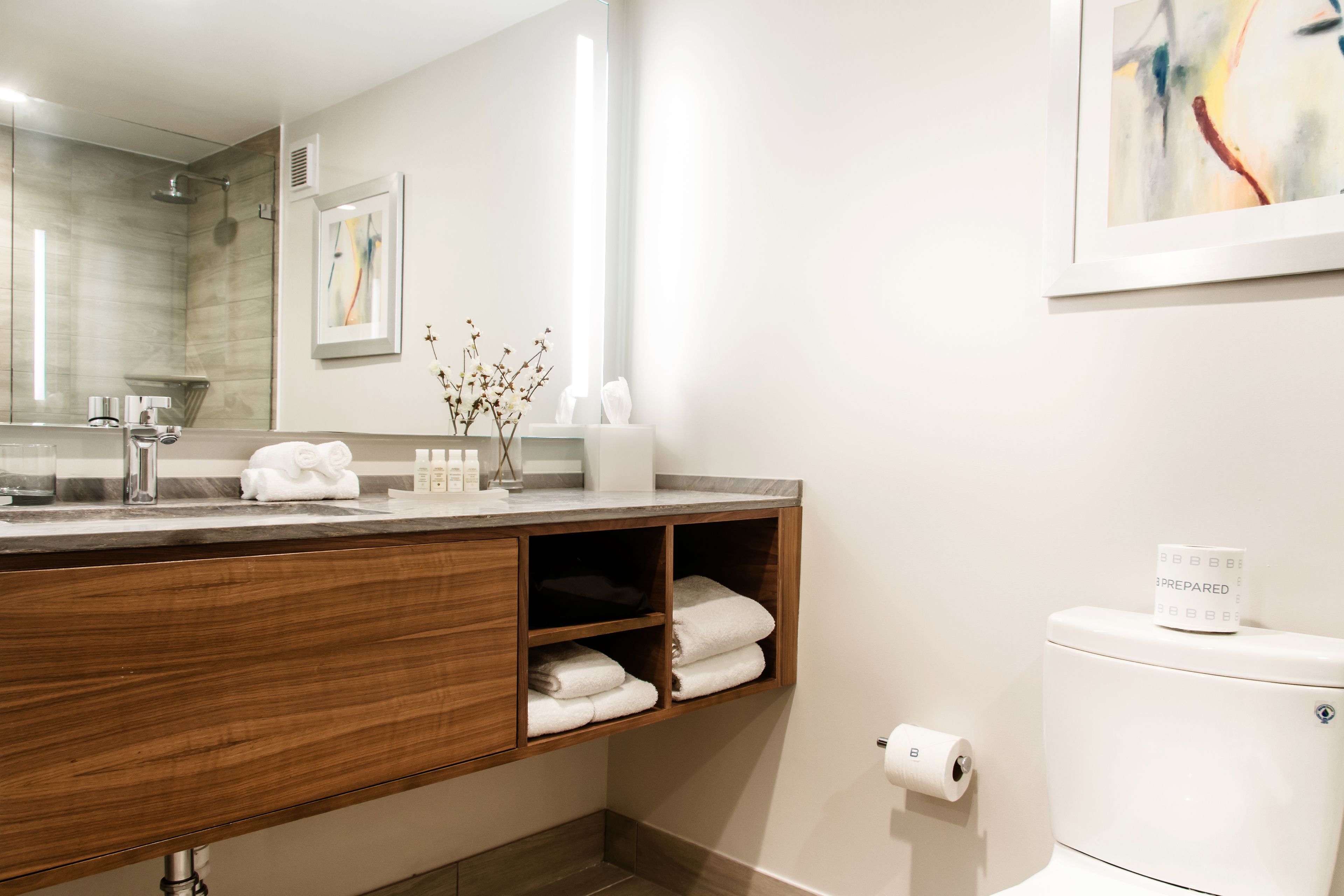 A modern bathroom with a wooden vanity, a large mirror, a shower, and a toilet.