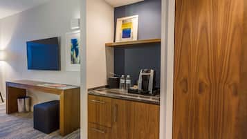 Una kitchenette compacta con cafetera, botellas de agua y una obra de arte enmarcada sobre la encimera.