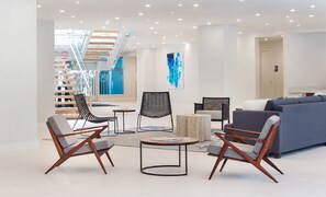 A modern living room with a grey sofa, two armchairs, a coffee table, and a staircase with glass railings.
