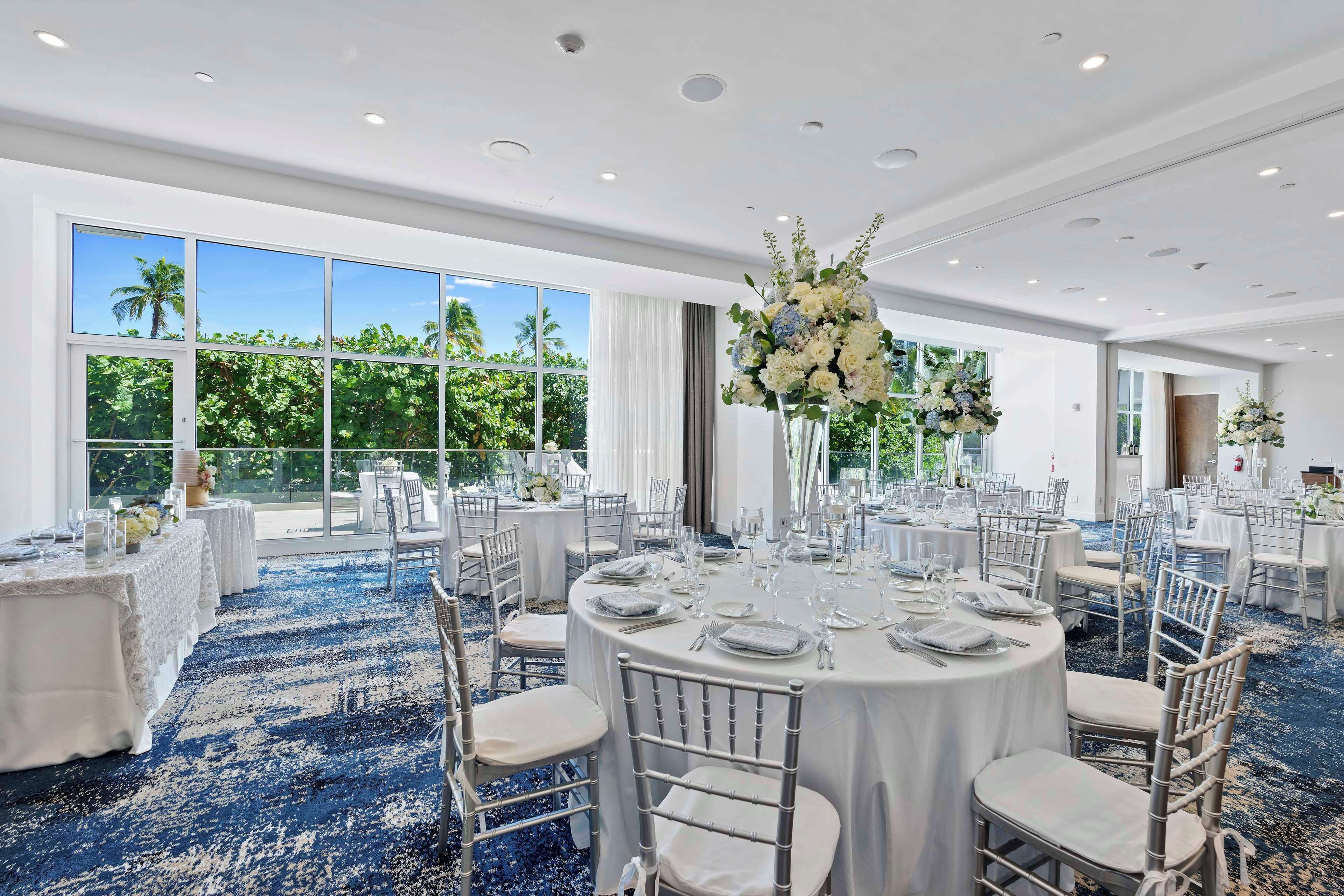 A banquet hall with round tables, white tablecloths, and silver chairs.