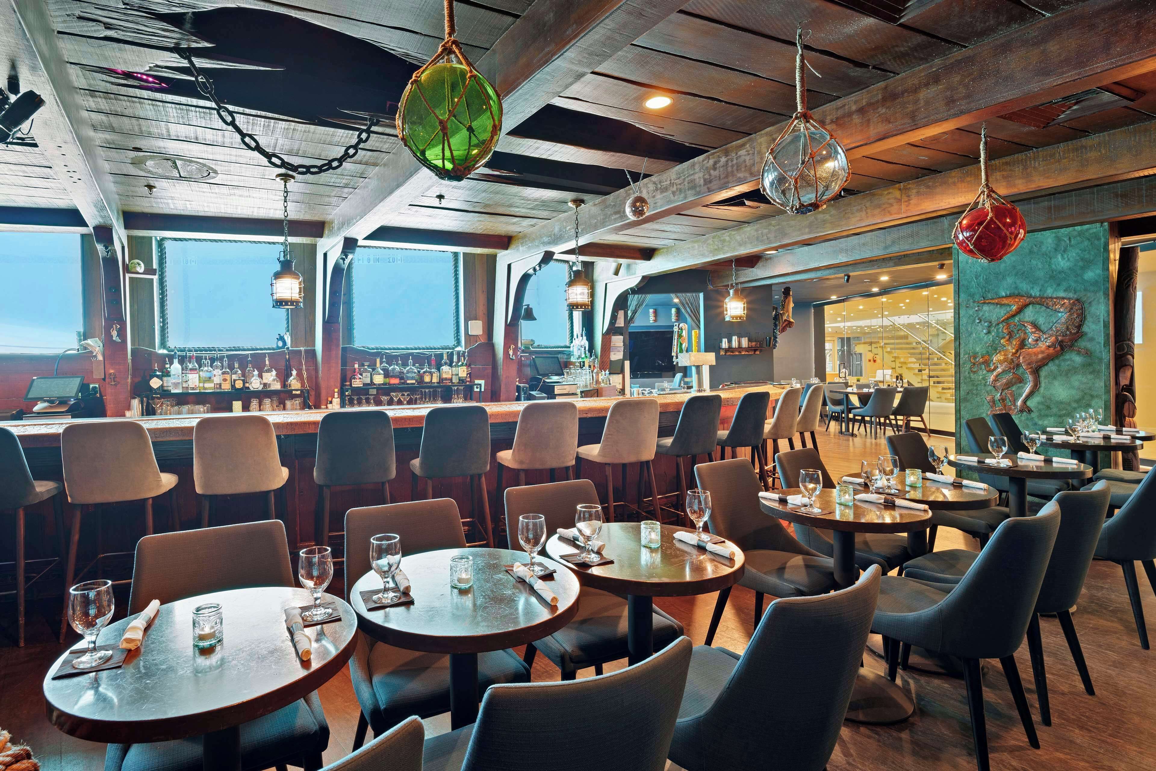 A restaurant with round tables and chairs, a bar area with bottles, and a mural on the wall.