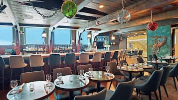 A restaurant with round tables and chairs, a bar area with bottles, and a mural on the wall.