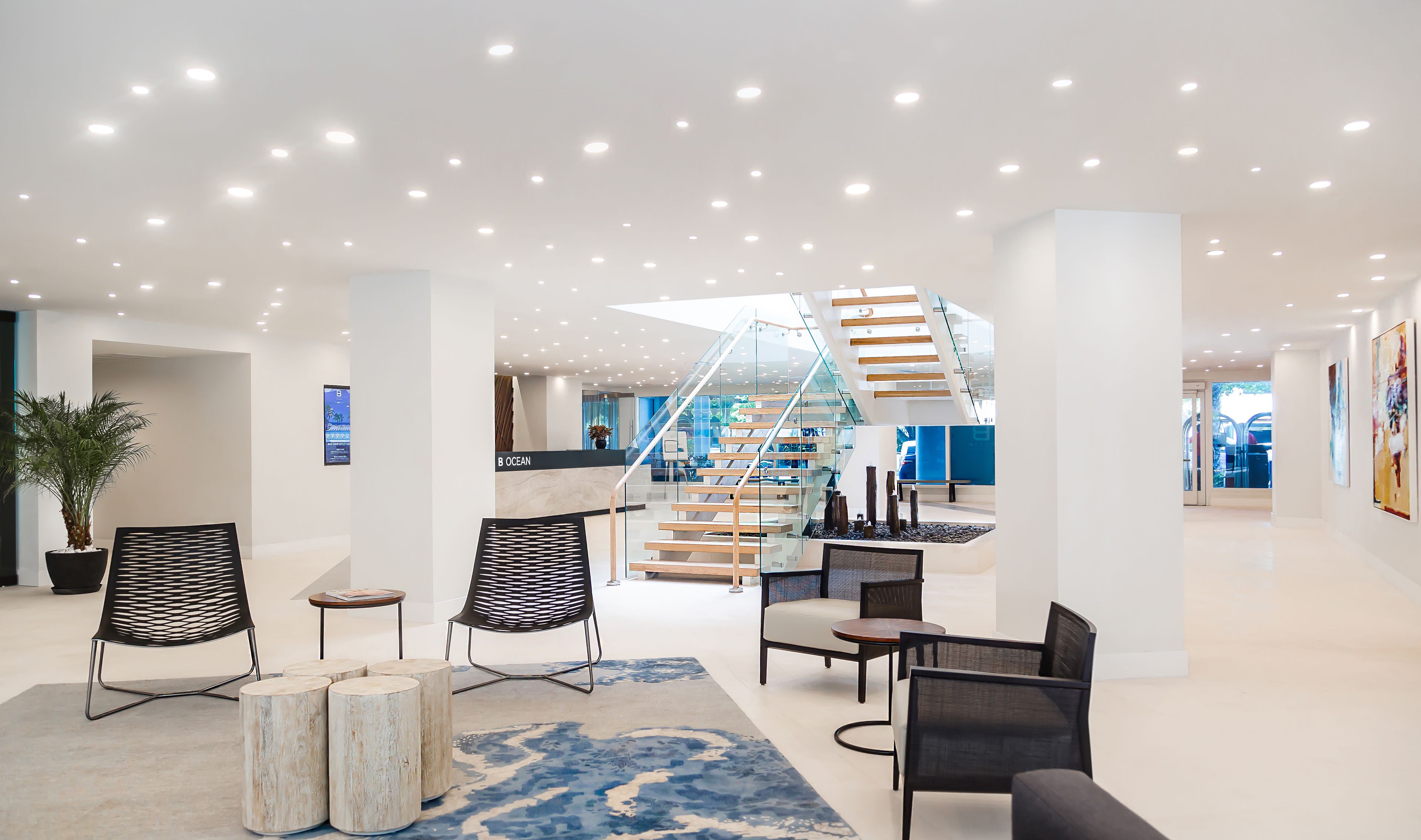 A spacious lobby with a modern staircase, seating areas, and a large potted plant.