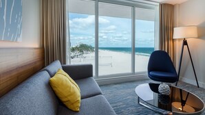 A hotel room with a grey sofa, a yellow pillow, a blue chair, a lamp, and a view of the beach. - B Ocean Resort Fort Lauderdale Beach (Fort Lauderdale)