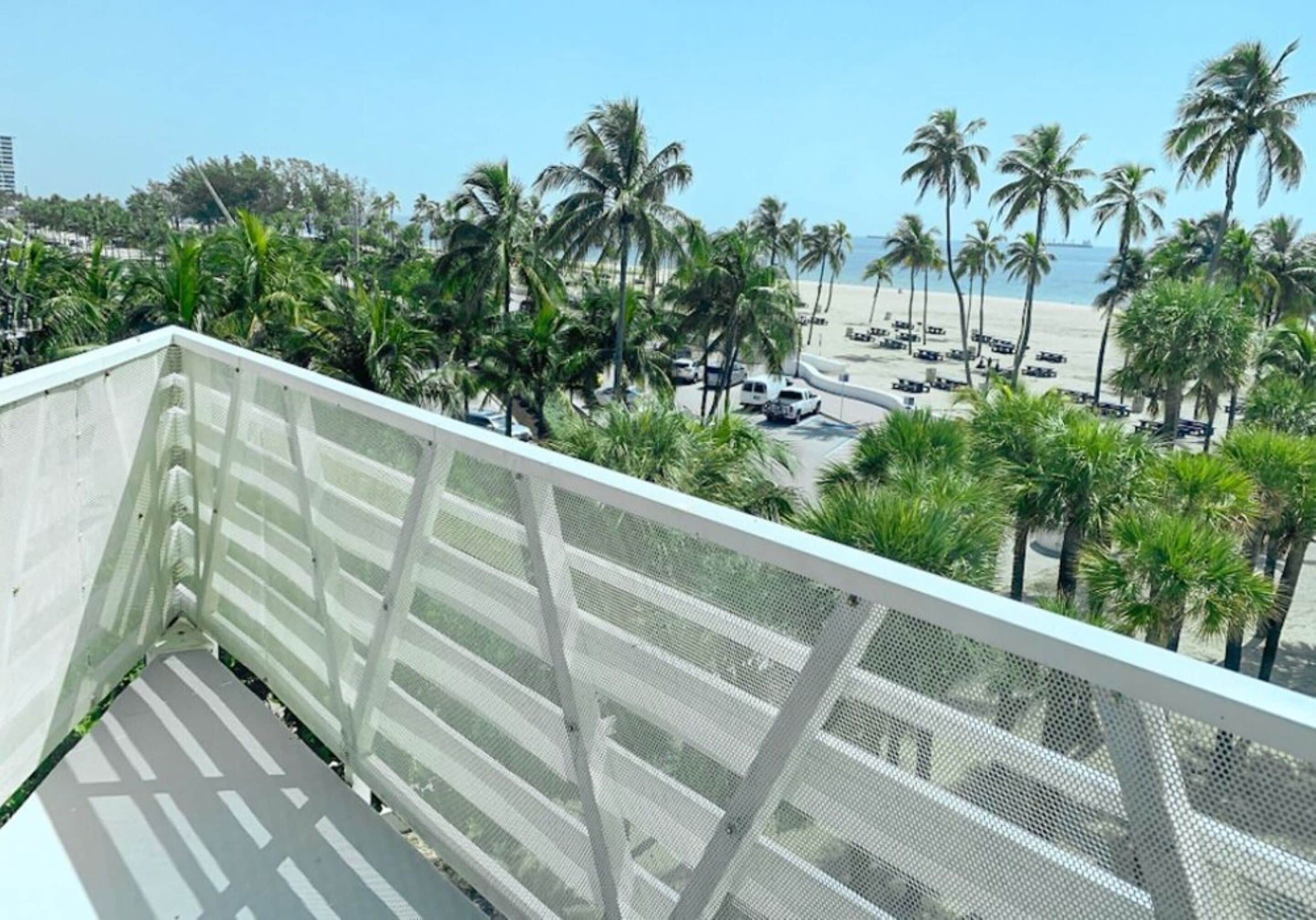Een balkon met uitzicht op een strand, palmbomen en geparkeerde auto's.