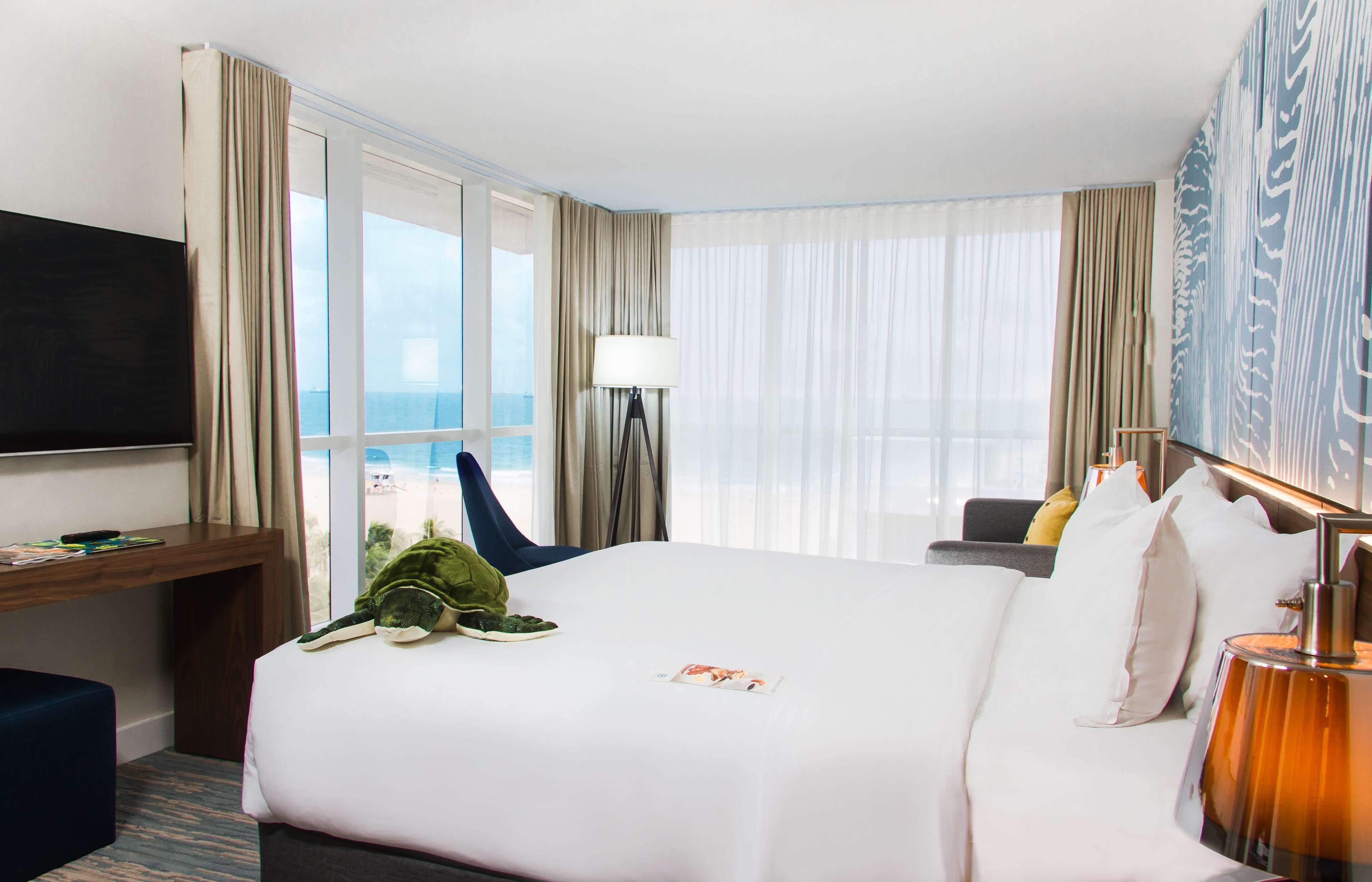 Habitación de hotel con una cama grande, un escritorio, un televisor y vista al océano.