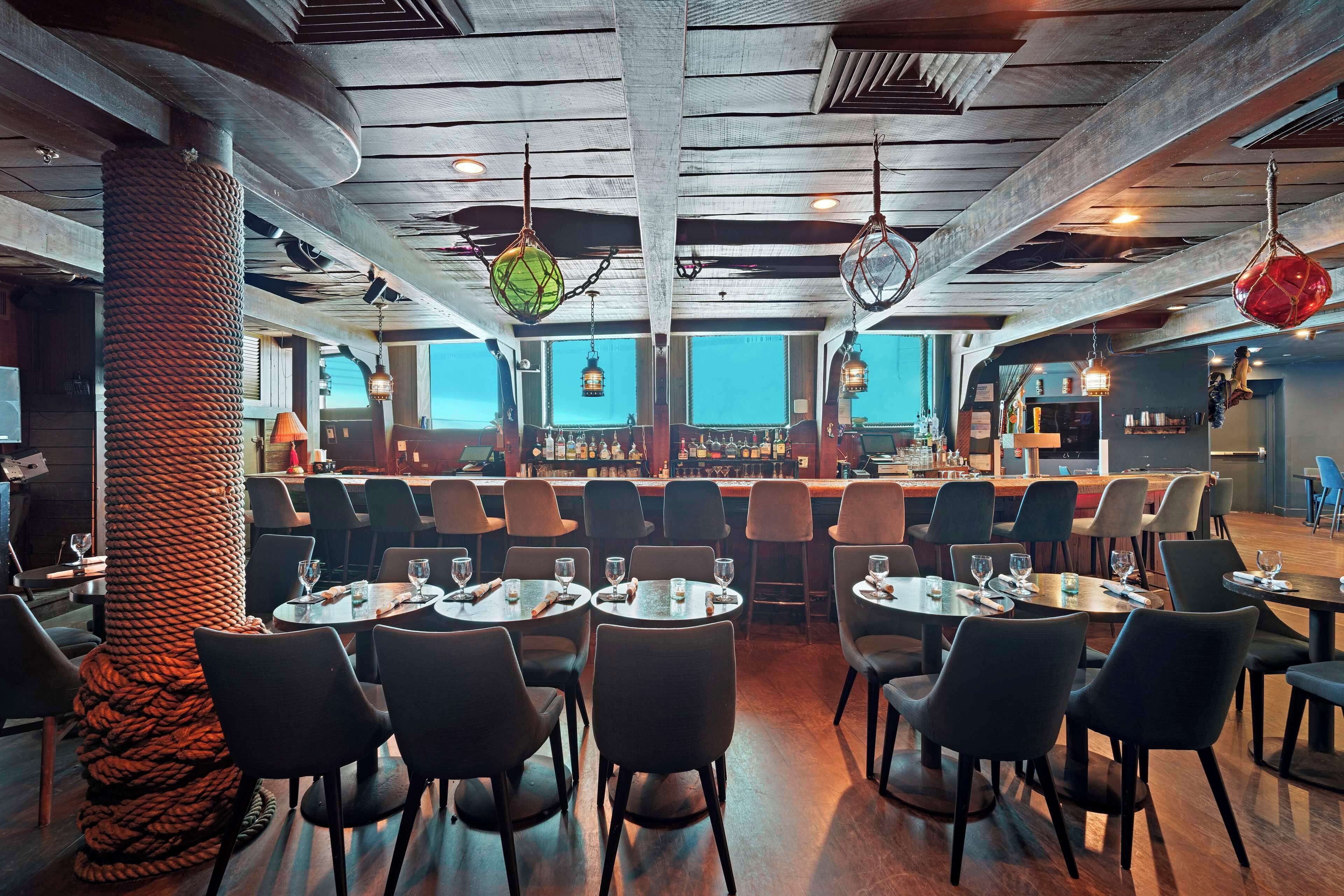 A restaurant with round tables and chairs, a bar area, and a large wooden column.