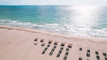 Uma praia com fileiras de cadeiras de salva-vidas laranja e uma orla arenosa.