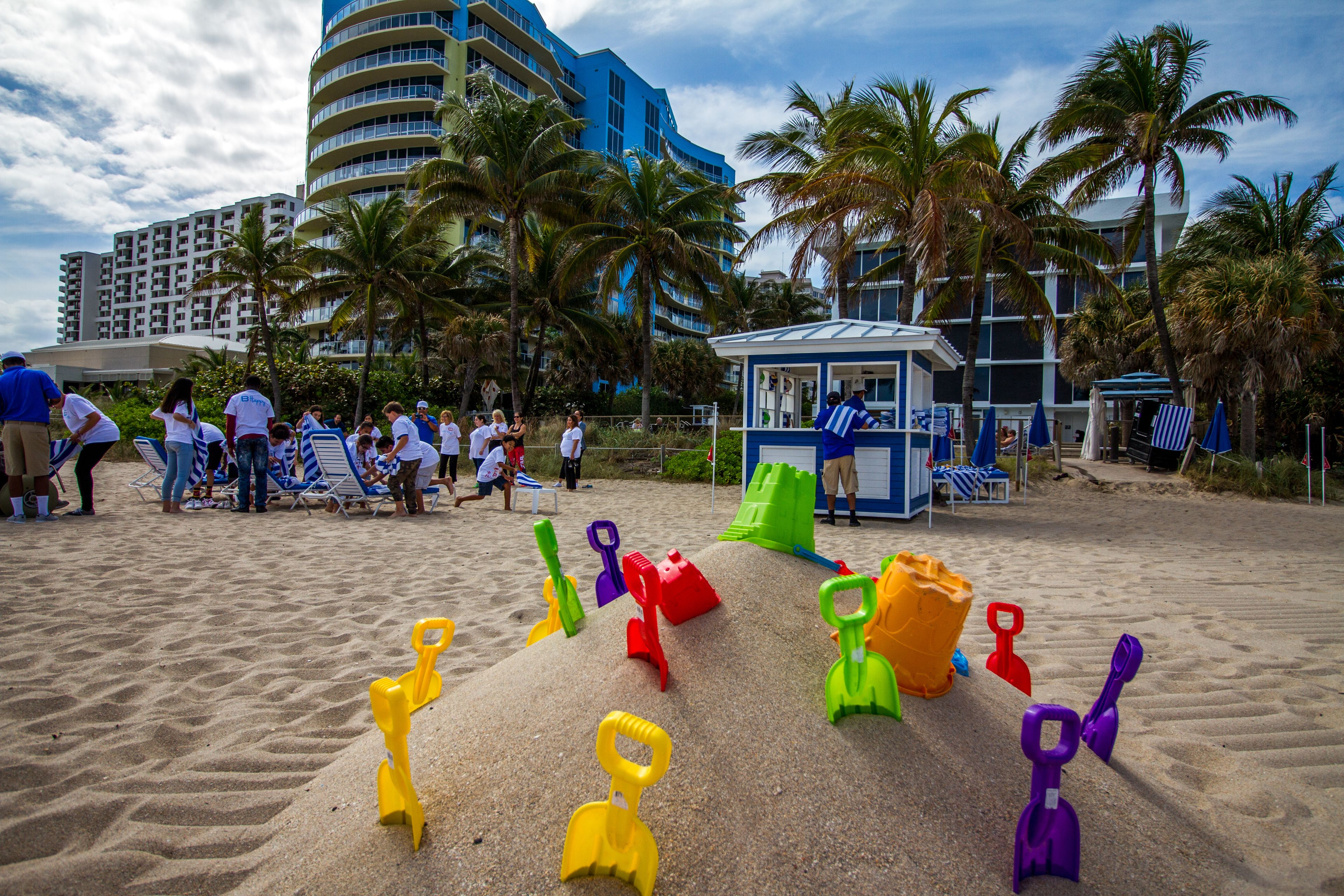 Una playa con juguetes de arena coloridos, palmeras y un edificio azul al fondo.