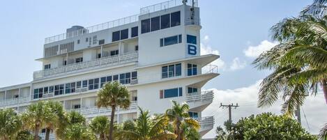 Un hotel de varios pisos con diseño moderno, que cuenta con balcones, ventanas amplias y un llamativo logotipo 'B' en la fachada.