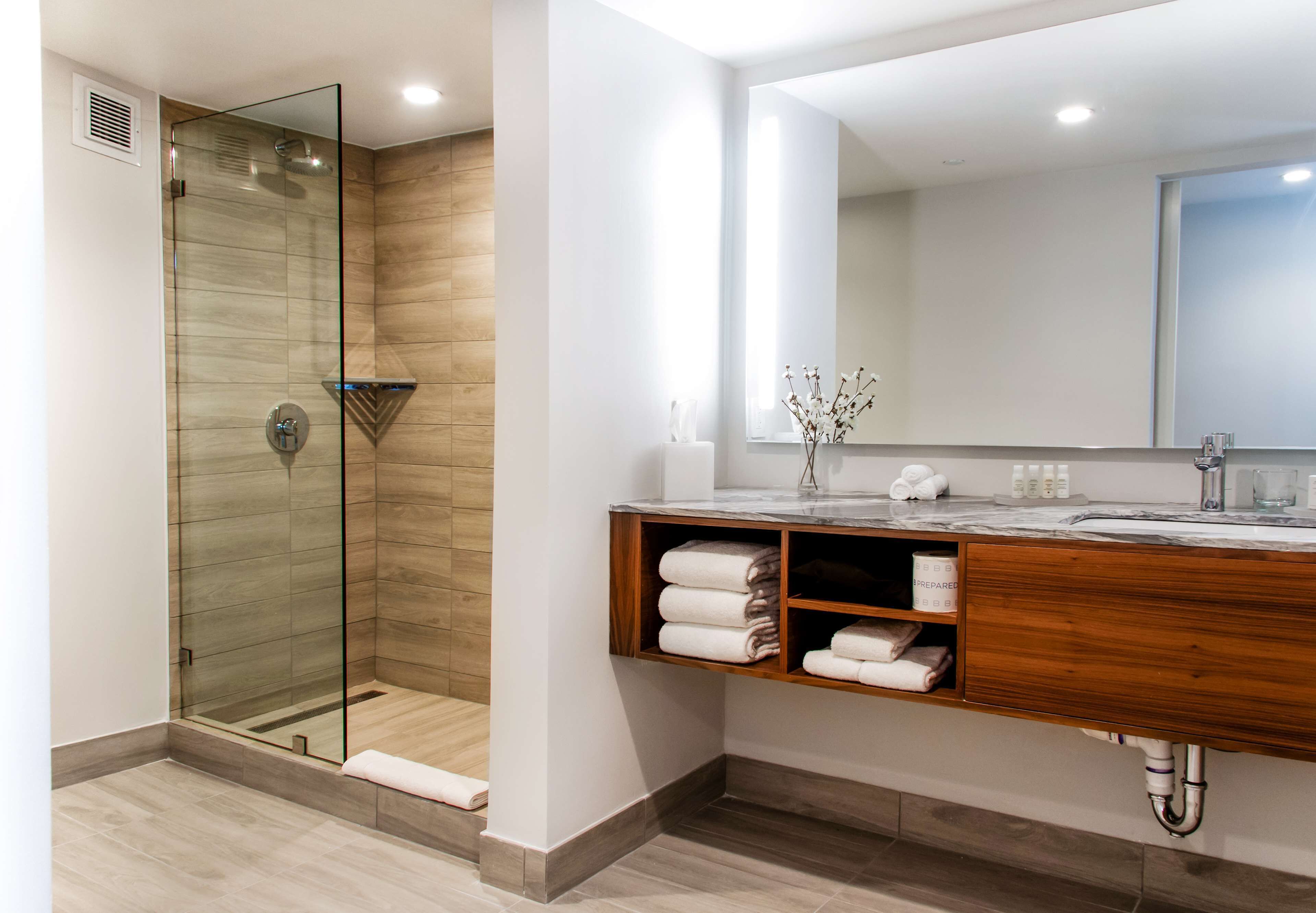 Un baño moderno con ducha de vidrio, tocador de madera y un espejo grande.