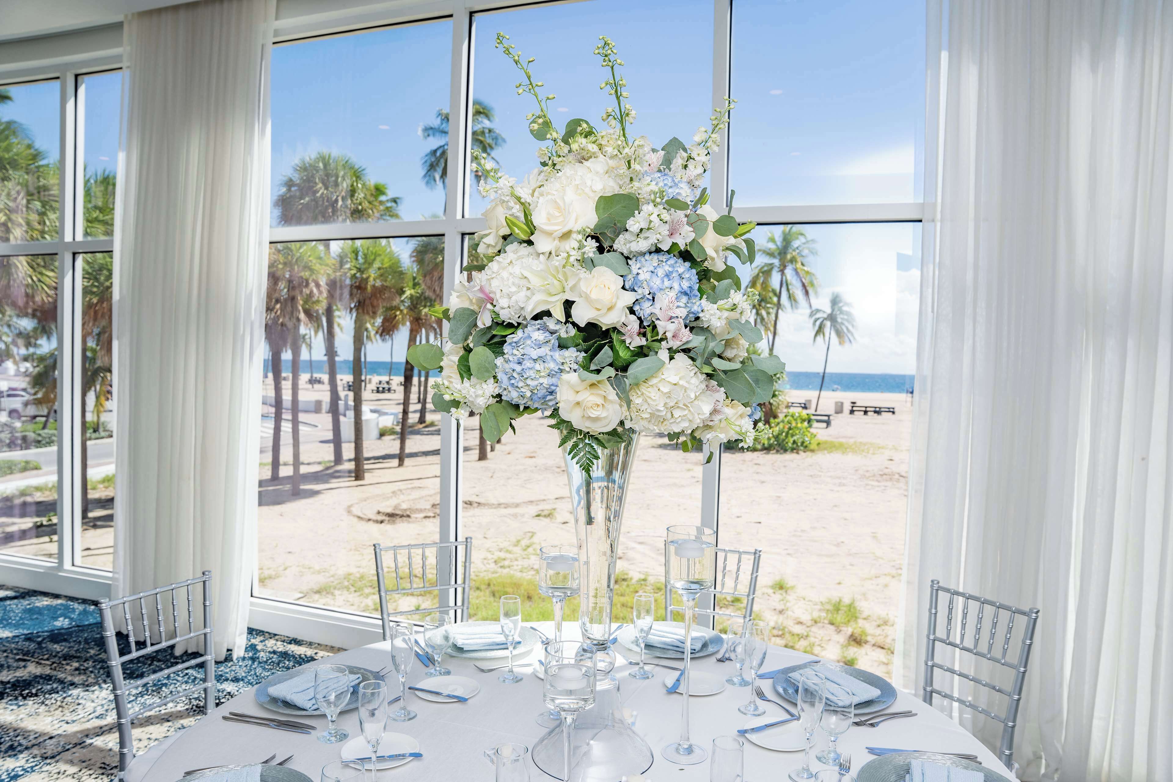 A table set for dining with a view of the beach and palm trees.