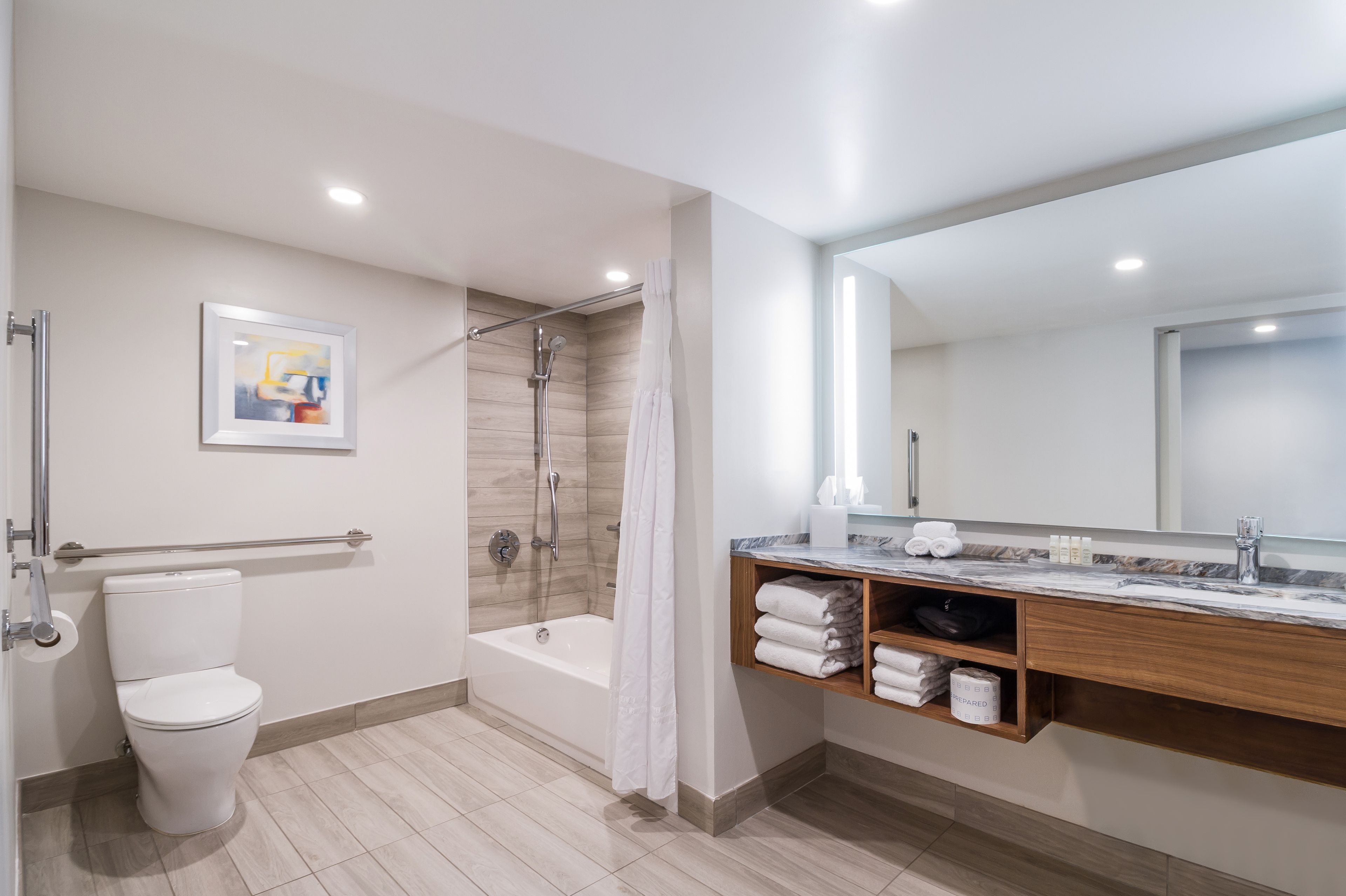 A modern bathroom with a toilet, shower, and bathtub. It includes a marble countertop and wooden shelves with towels.