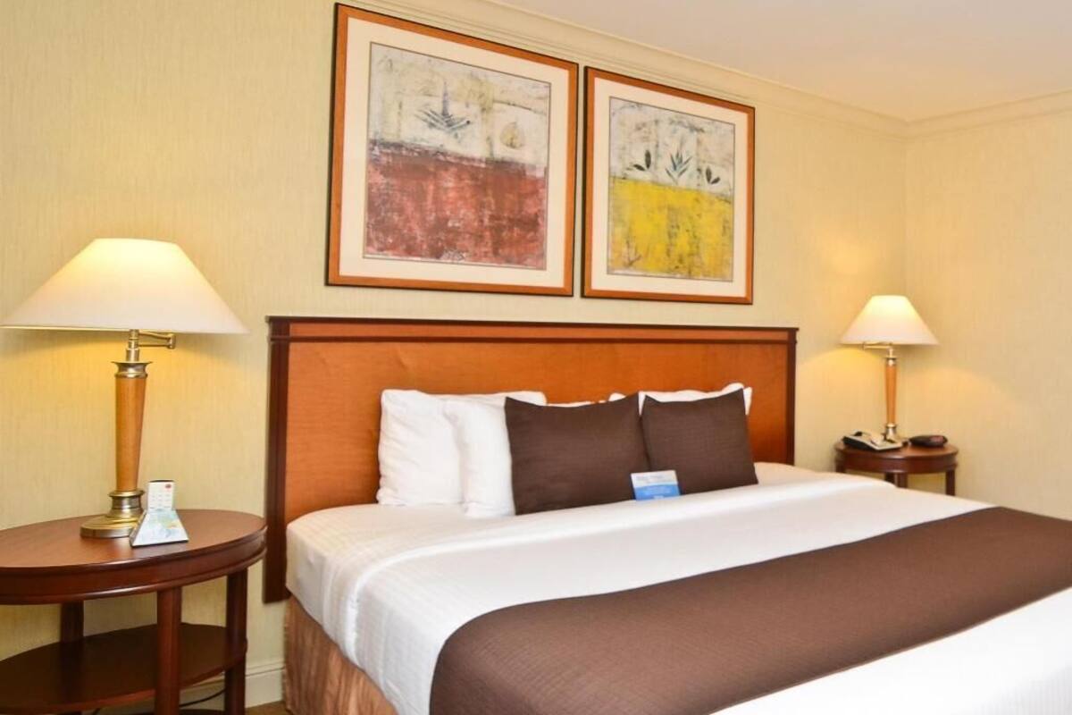 Ein Hotelzimmer mit einem großen Bett, zwei Nachttischen und zwei gerahmten abstrakten Bildern an der Wand.
