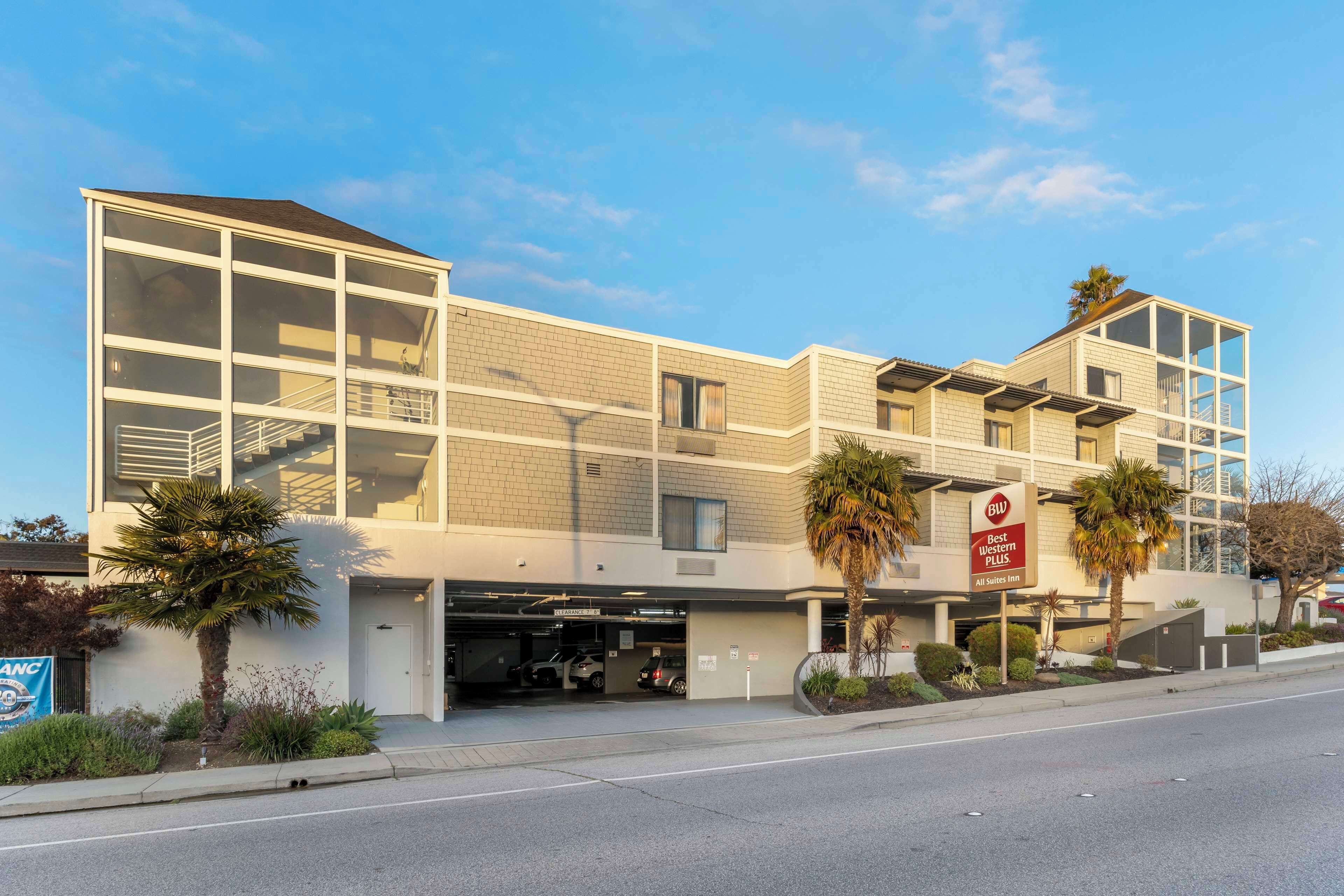 A modern hotel with a glass facade, a parking garage, and palm trees.