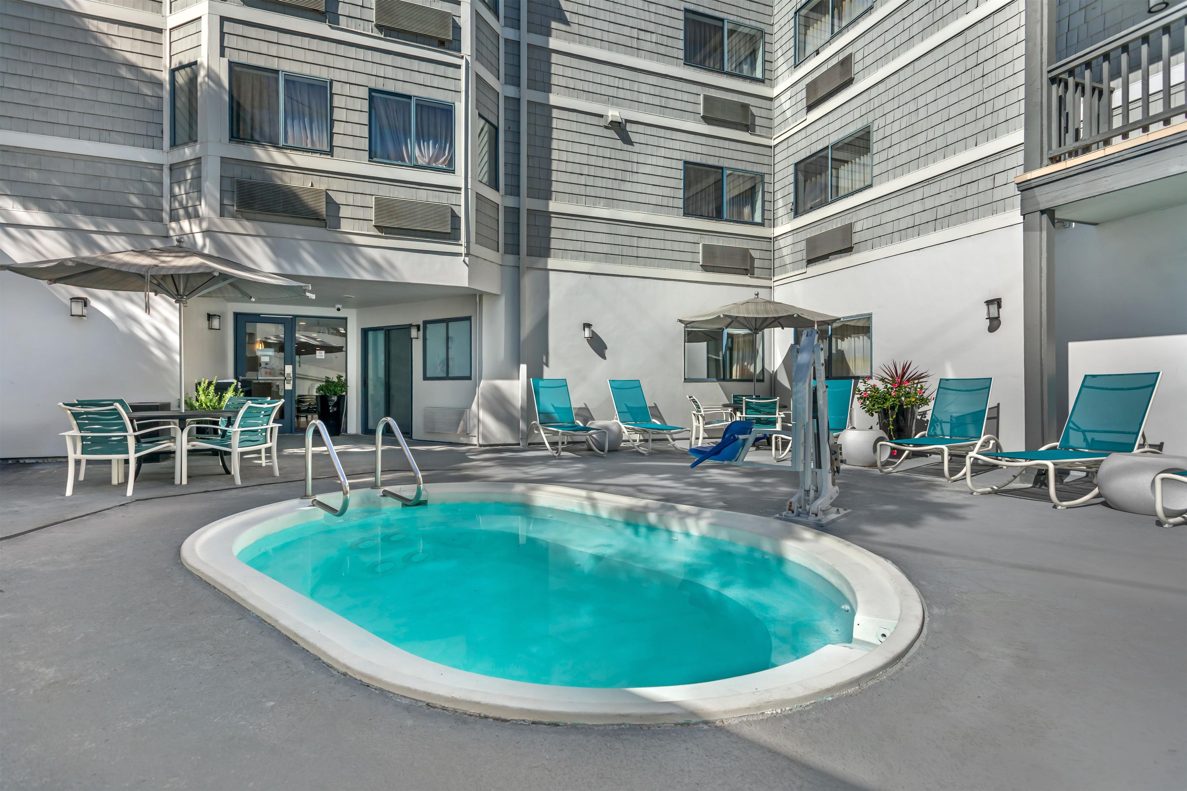 A pool area with a hot tub, lounge chairs, and a dining area with tables and chairs.