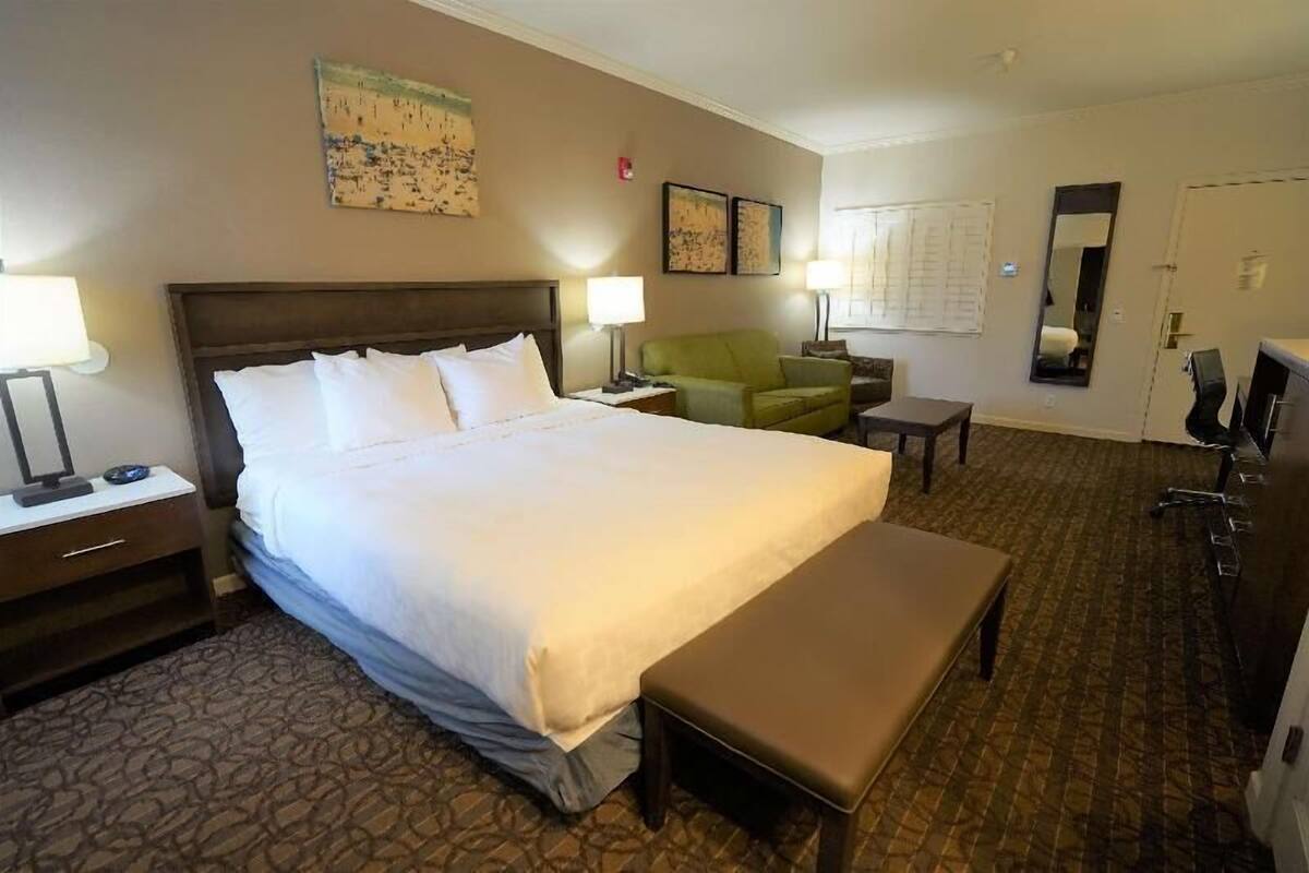 Ein Hotelzimmer mit einem großen Bett, Nachttischen, einem grünen Sessel, einem kleinen Tisch, einer Bank und einem Spiegel.