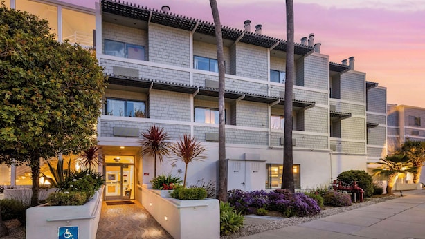 A multi-story hotel with a modern design, featuring a landscaped entrance with plants and a wheelchair-accessible sign. - Best Western Plus All Suites Inn (Santa Cruz)
