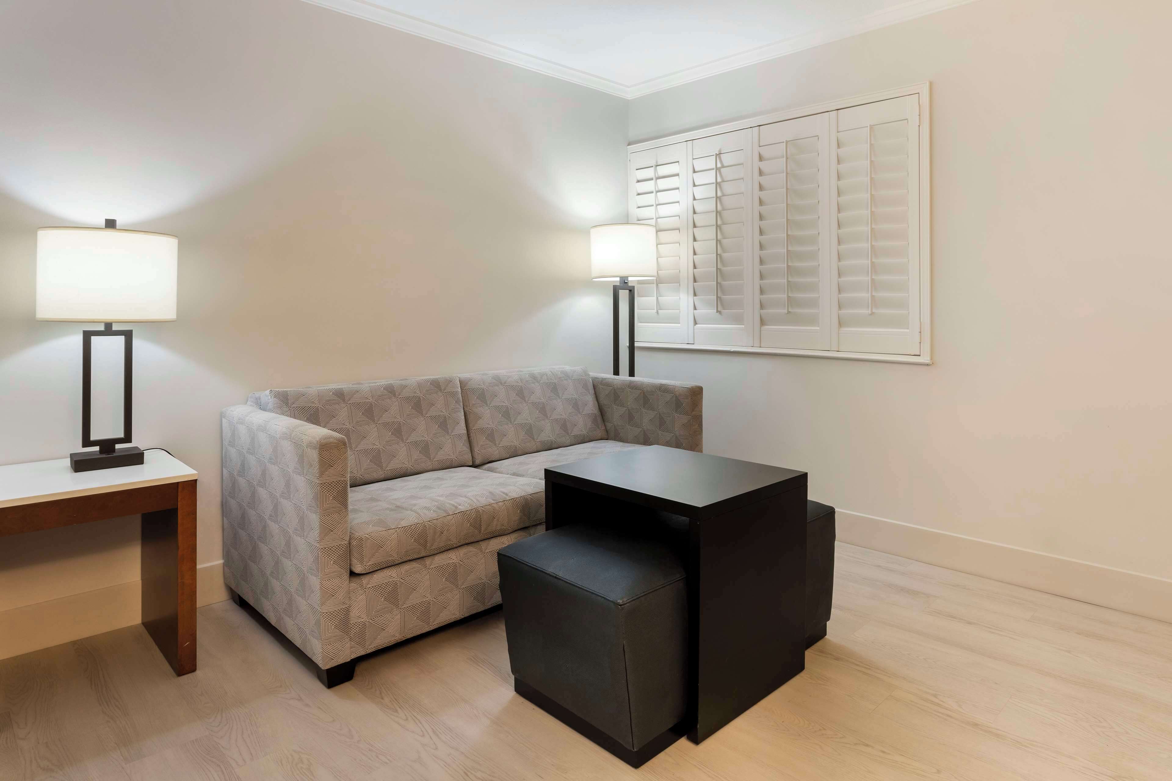 A modern living room with a sofa, a small black ottoman, a wooden side table, and two floor lamps.