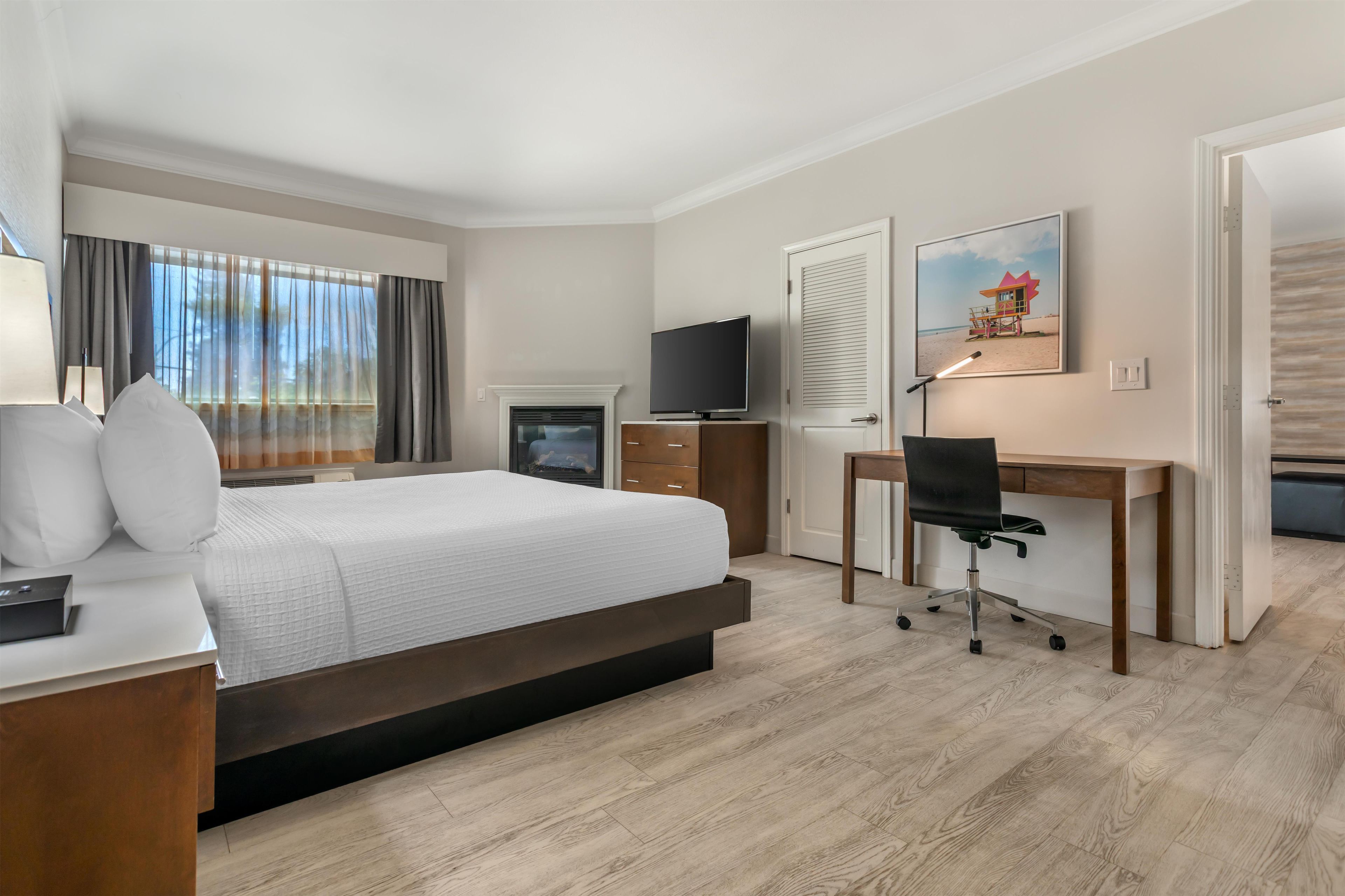 A hotel room with a bed, a desk, a television, and a painting on the wall.