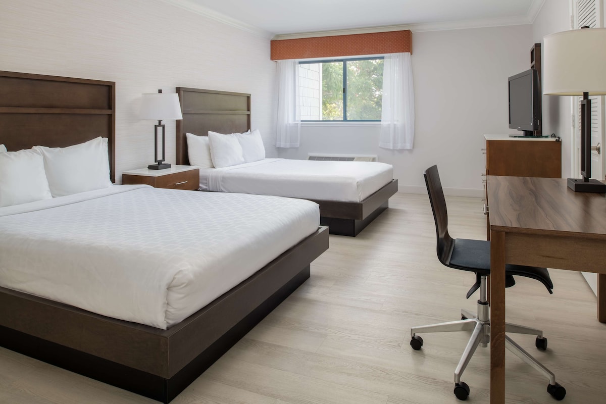 Ein Hotelzimmer mit zwei Betten, einem Schreibtisch, einem Stuhl, einem Fernseher und einem Fenster mit Vorhängen.