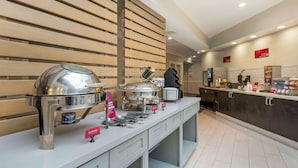 A buffet setup with various food containers and utensils, a person in the background, and a modern interior design. - Best Western Plus All Suites Inn (Santa Cruz)
