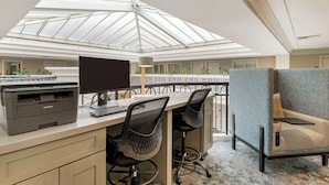 A modern office space with a large skylight, a Brother printer, two ergonomic chairs, a desk, and a blue upholstered armchair. - Best Western Plus All Suites Inn (Santa Cruz)