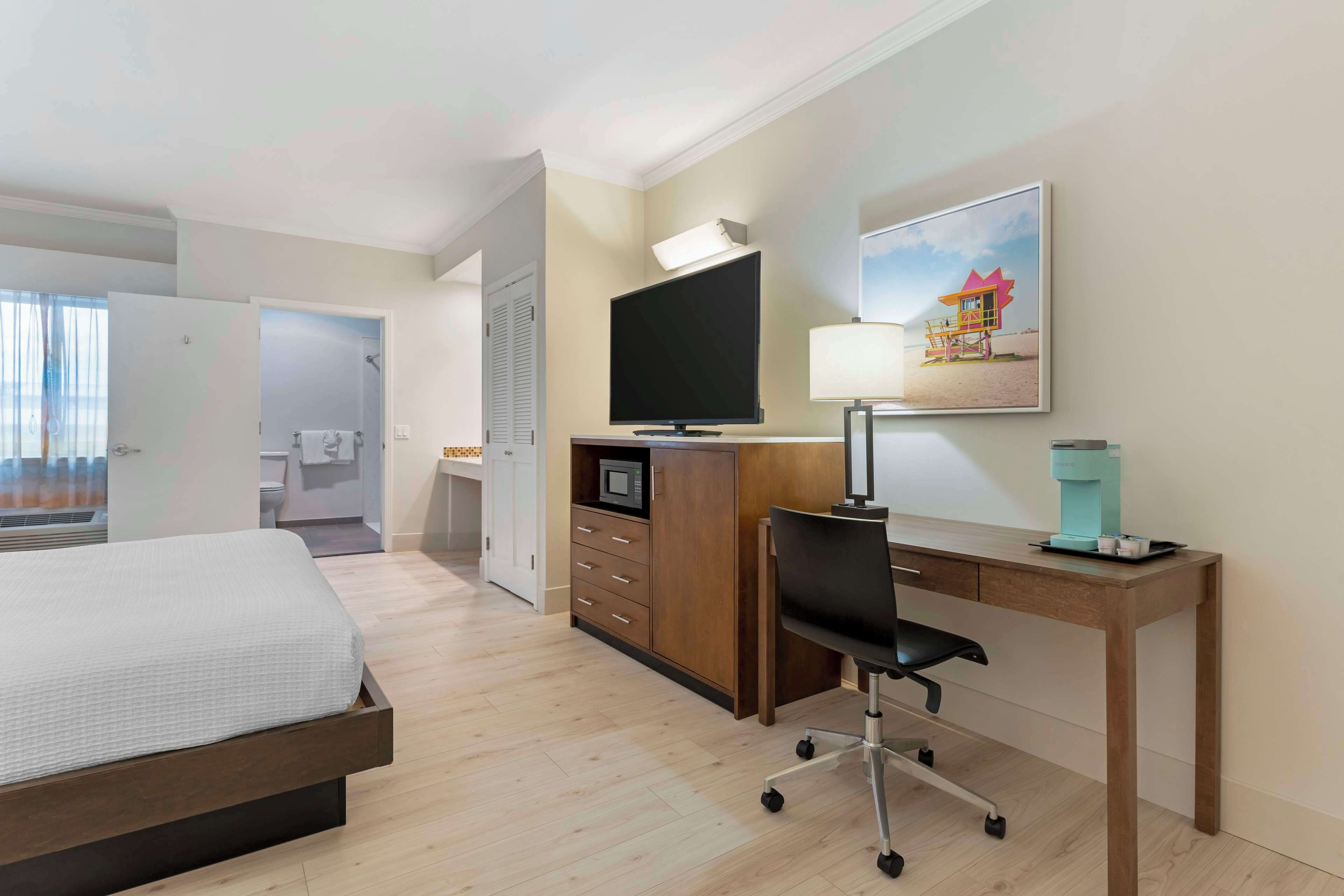 Ein Hotelzimmer mit einem Bett, einem Schreibtisch mit Computer, einem Fernseher, einer Kaffeemaschine und einem Bild an der Wand.
