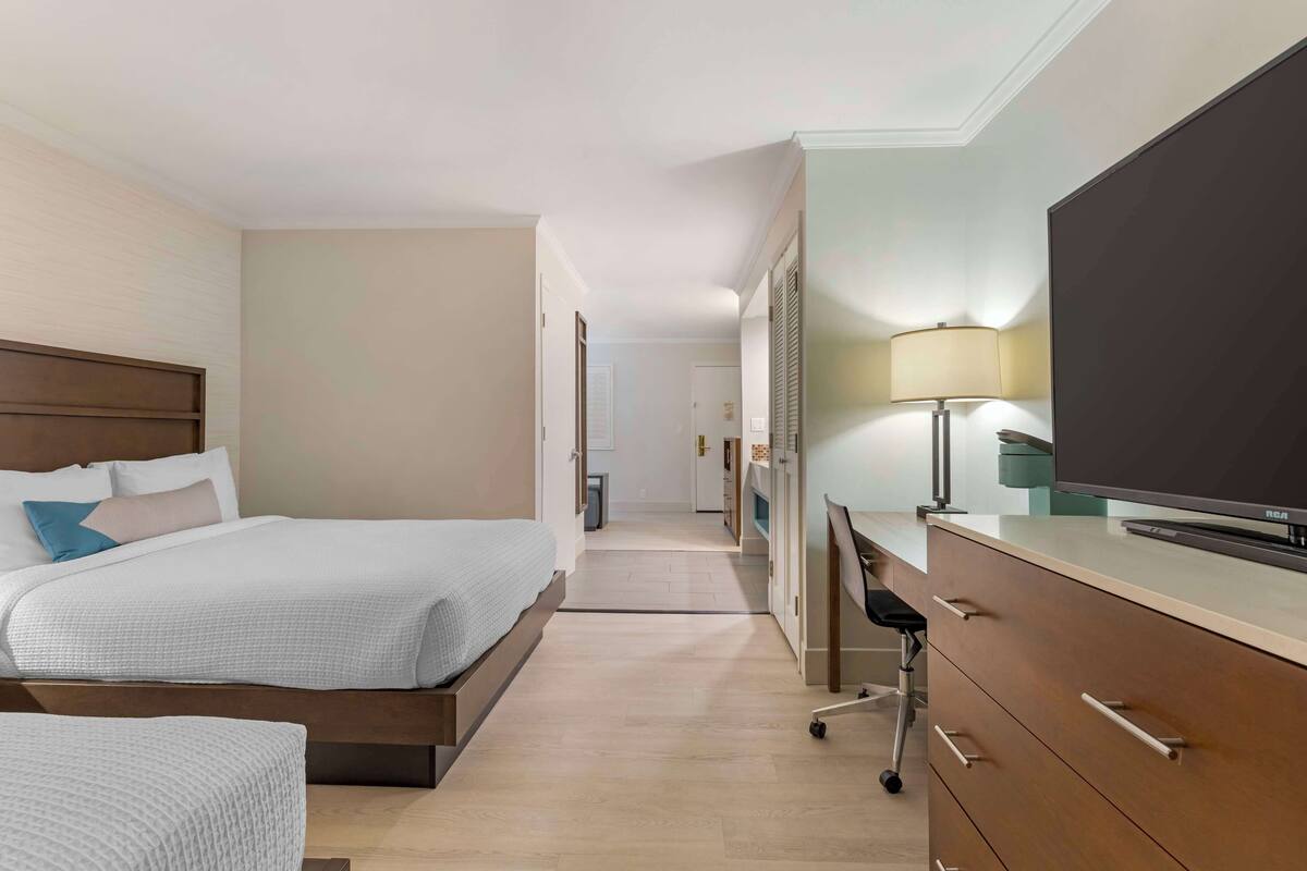 Ein Hotelzimmer mit zwei Betten, einem Schreibtisch mit Fernseher und einer Lampe.