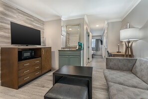 A modern living room with a flat-screen TV, a coffee machine, a sofa, and a dining area with a lamp. - Best Western Plus All Suites Inn (Santa Cruz)
