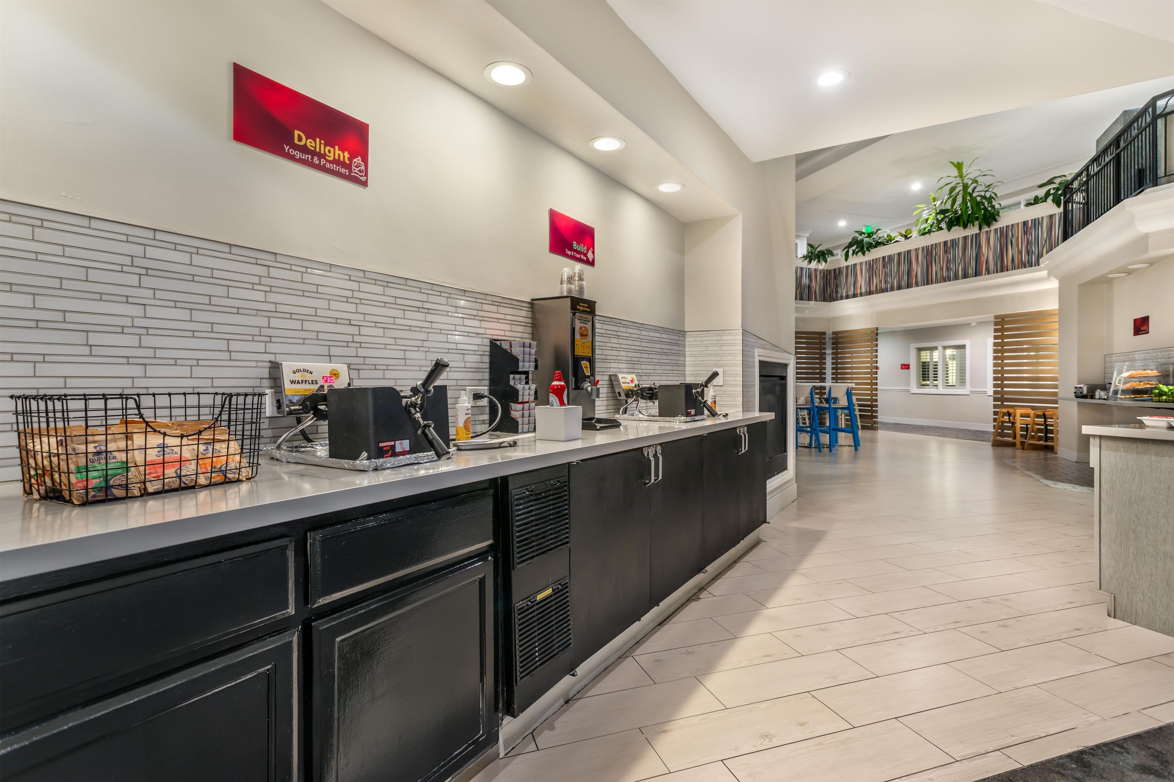 A modern kitchen area with a counter, coffee machines, and a sign for 'Delight Yogurt & Pastries'.