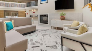 A spacious living area with a beige sectional sofa, a white armchair, and a patterned rug. A flat-screen TV is mounted on the wall, and a fireplace is visible in the background. - Best Western Plus All Suites Inn (Santa Cruz)