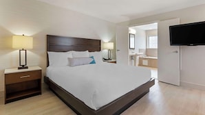 A modern hotel room with a large bed, bedside lamps, a flat-screen TV, and a bathroom visible through an open door. - Best Western Plus All Suites Inn (Santa Cruz)