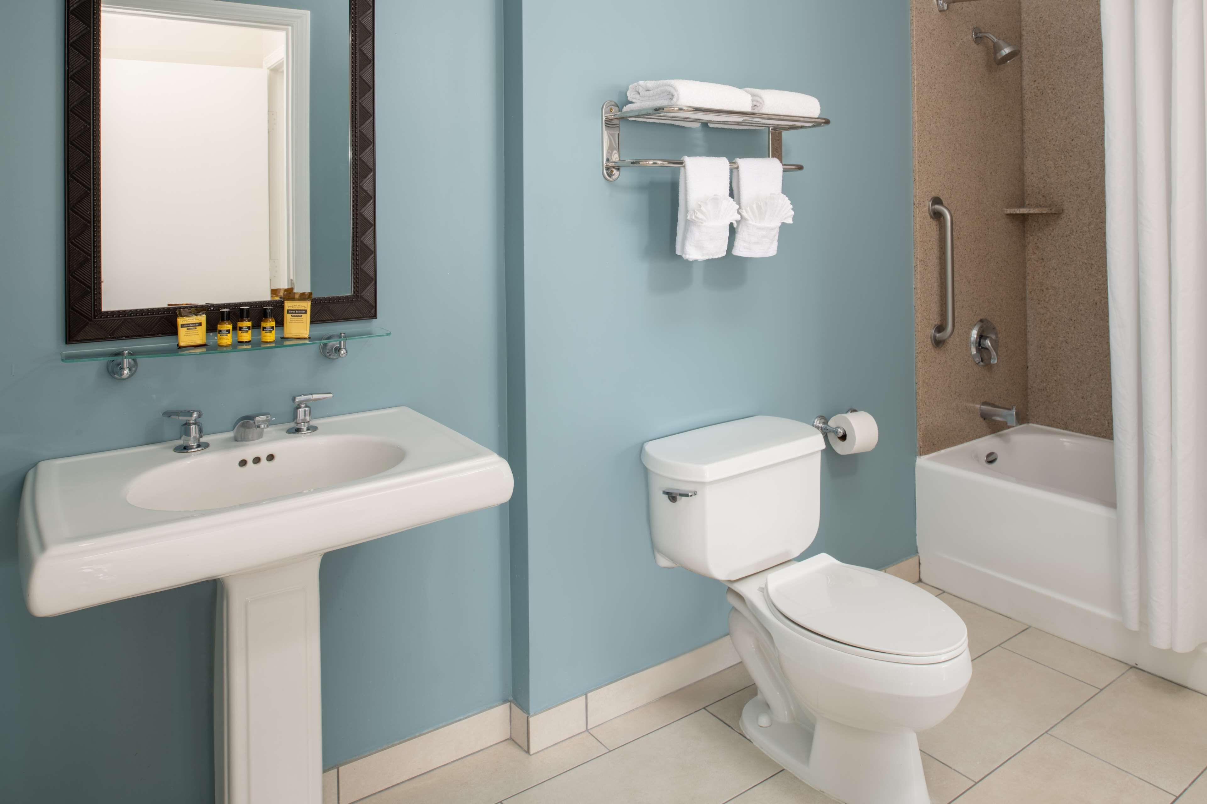 Ein Badezimmer mit einem weißen Waschbecken, einer Toilette, einer Glasablage für Toilettenartikel und einer Duschkabine.
