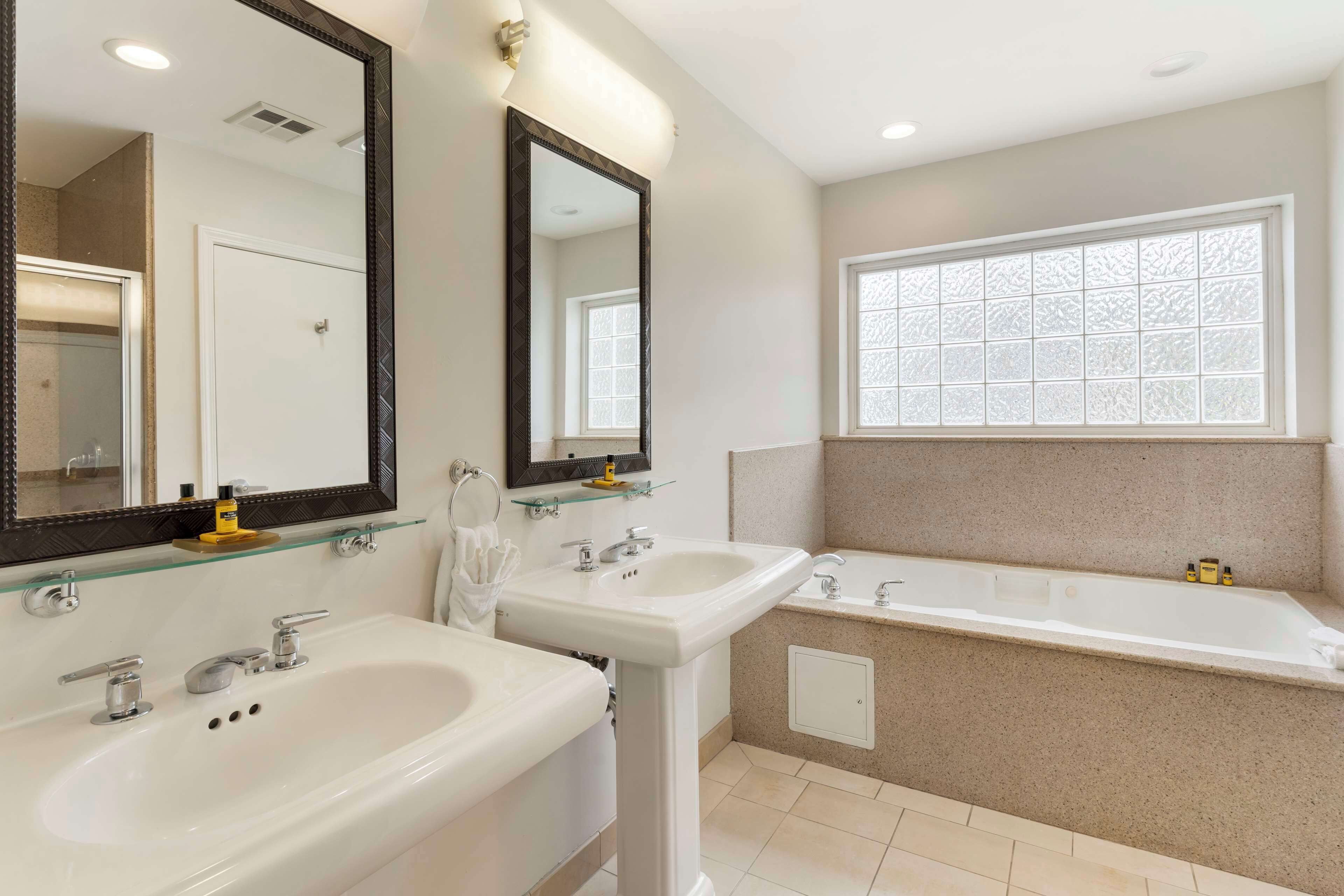 A modern bathroom with two sinks, a large bathtub, and a window with frosted glass.