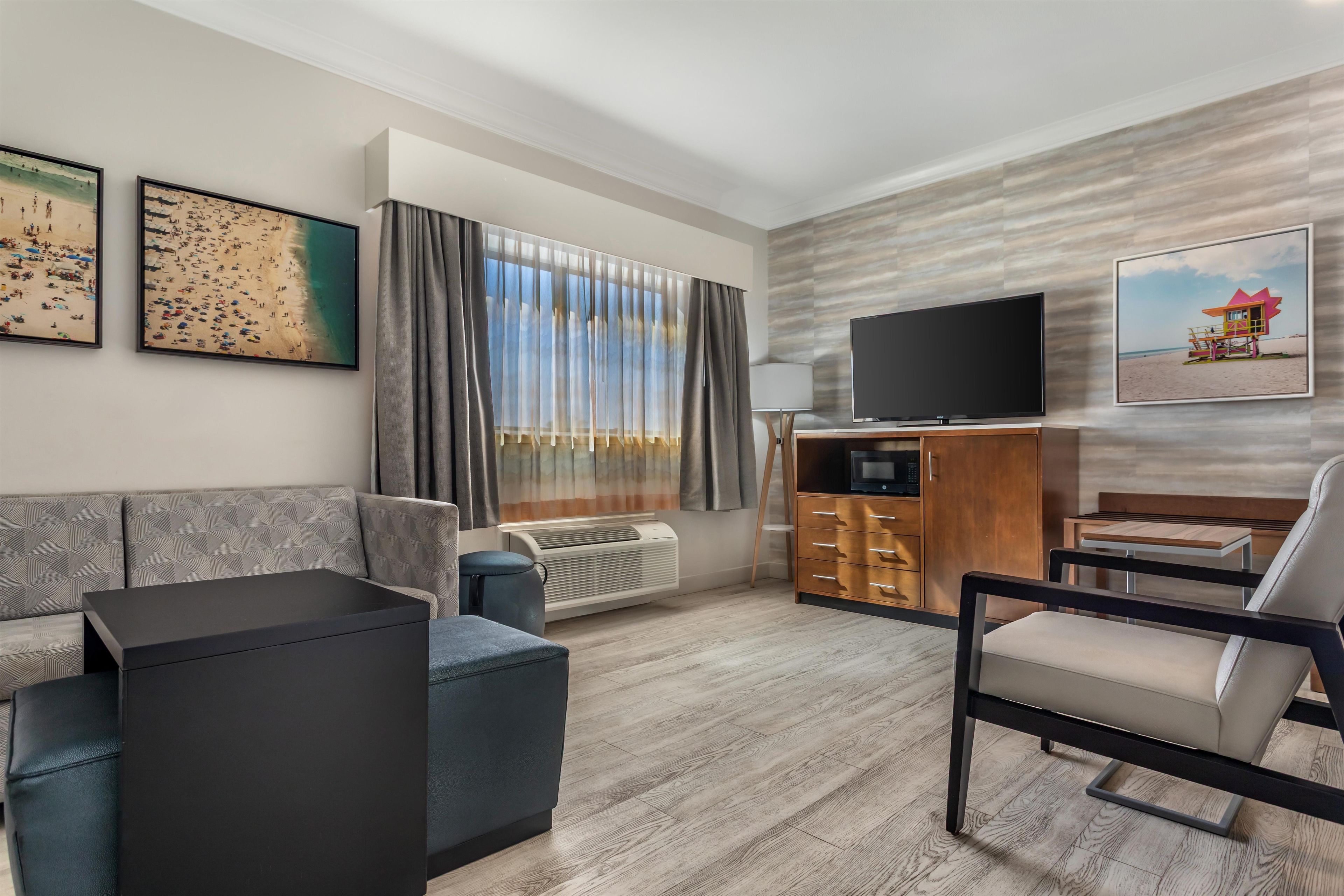 A modern hotel room with a sofa, a chair, a flat-screen TV, a small table, and a cabinet.