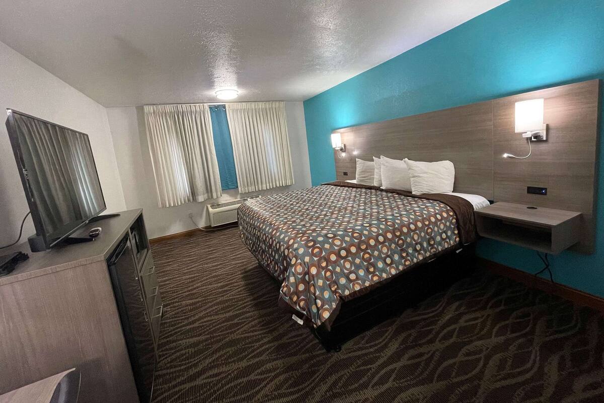 Ein Hotelzimmer mit Bett, Fernseher, Schreibtisch und einem Fenster mit Vorhängen.